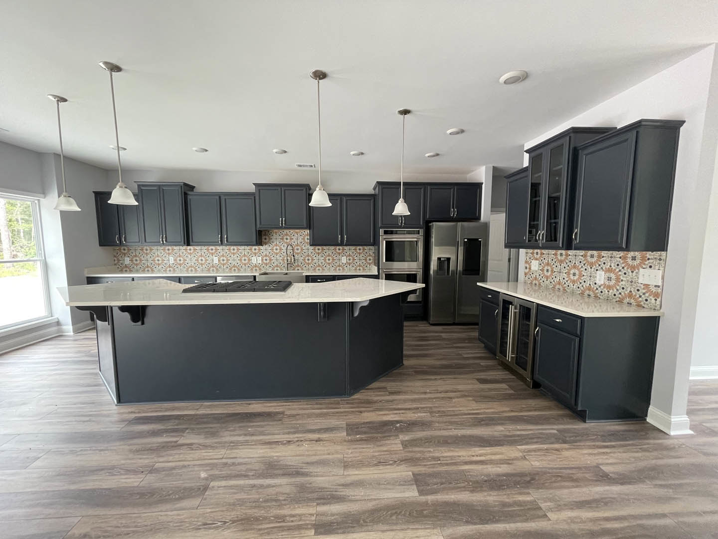 Spacious kitchen featuring a large central island with black cabinetry, white countertops, stainless steel refrigerator, white walls accented by black trim, tile flooring, and a