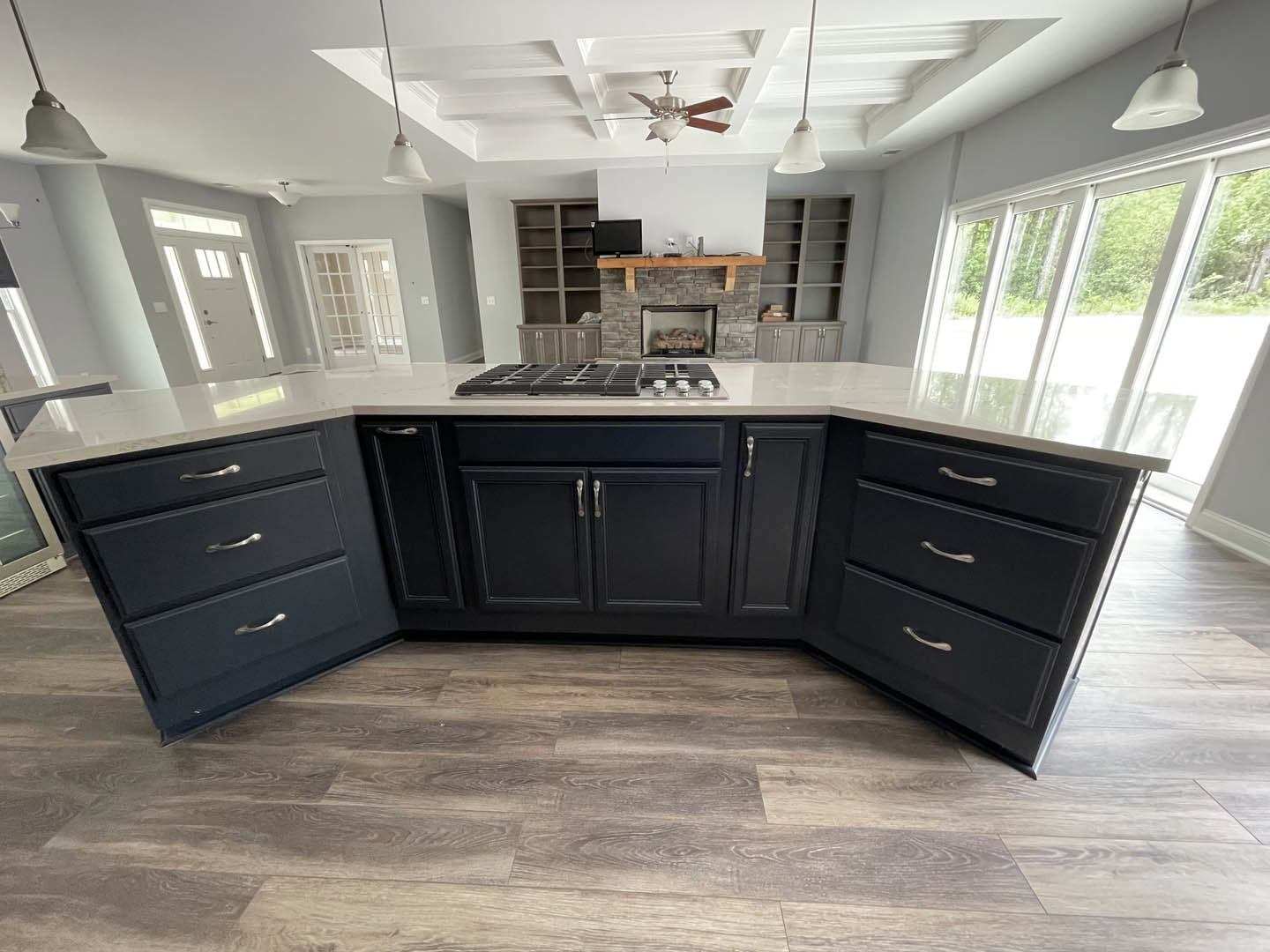 Kitchen with wood flooring, ceiling fan, white cabinetry, glass-paneled door, stainless steel stovetop, and light fixture above countertops