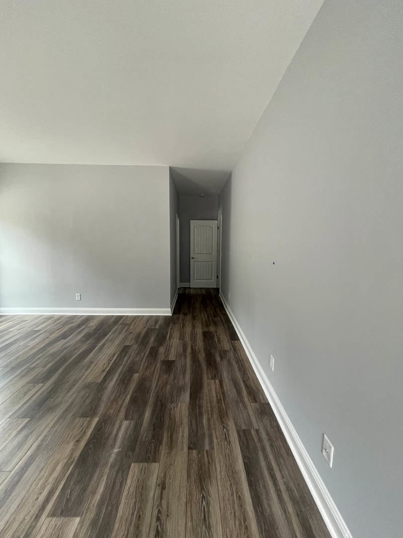 Wood floor with natural grain pattern, white walls, and a white door featuring a silver handle in a residential interior.