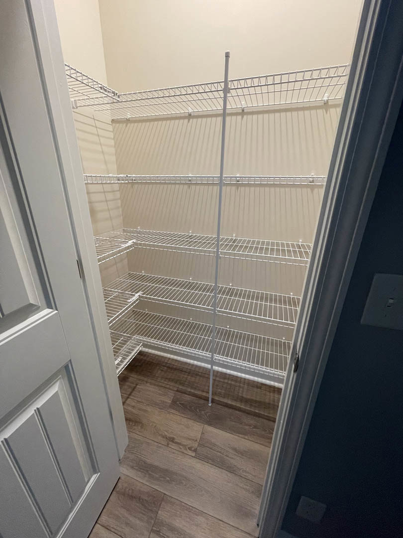 Walk-in closet with white built-in shelves, wood flooring, and a white paneled door