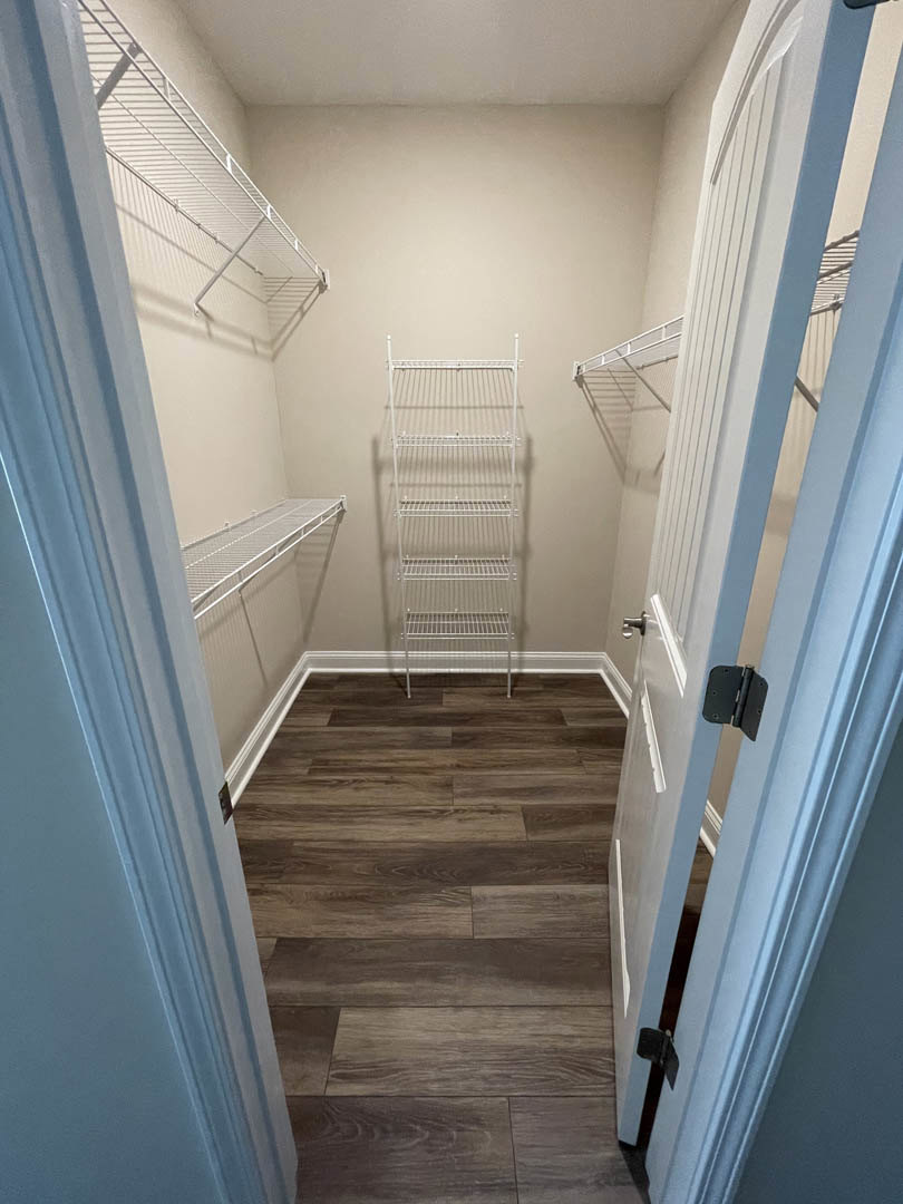 Closet with white wire shelving, wood floor, white door with black hinge, and white walls