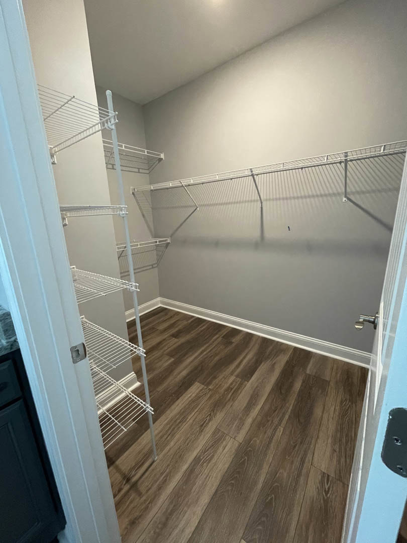 Walk-in closet with white built-in shelves, wood flooring, and white baseboard trim
