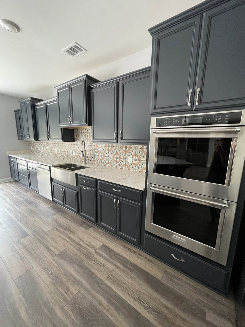 Grey shaker cabinets, stainless steel refrigerator and oven, white quartz countertops, light wood flooring, recessed ceiling vent, subway tile backsplash