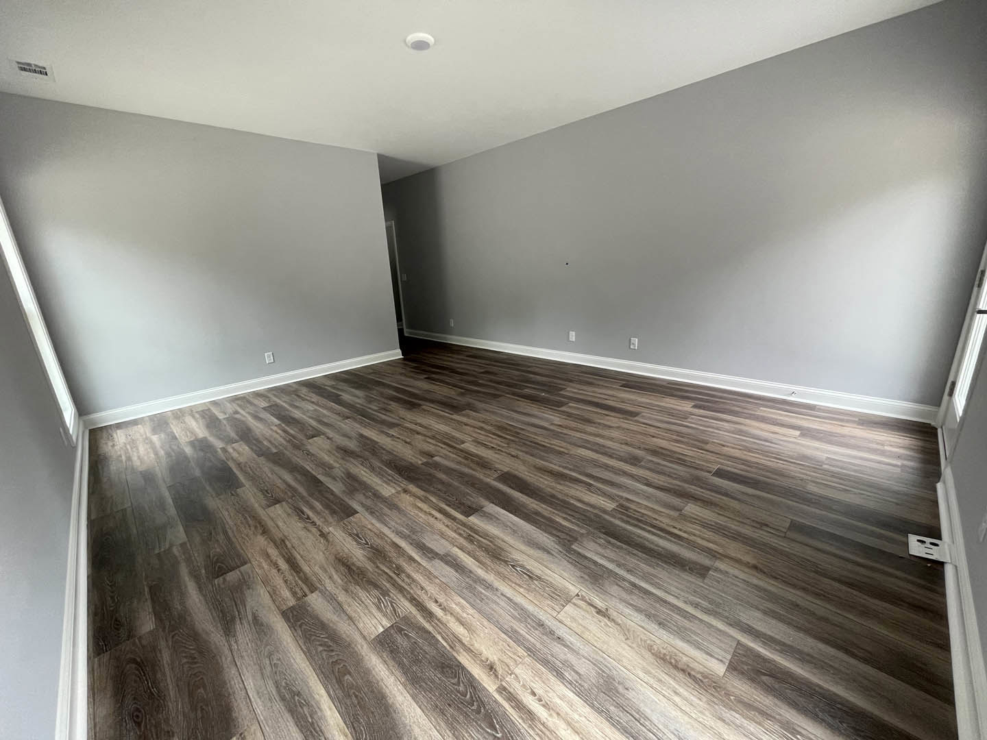 Wood flooring in a spacious room with white plaster walls, white ceiling, recessed lighting, and a rectangular vent on the wall.