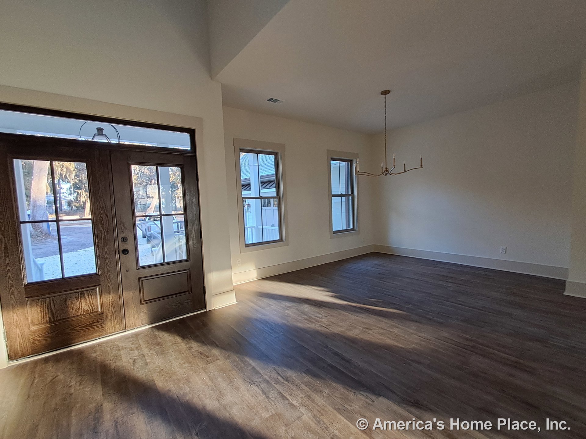 Double wooden front doors with transom window, wide plank wood flooring, neutral wall trim and baseboards, dining area featuring modern chandelier, multiple large windows providing