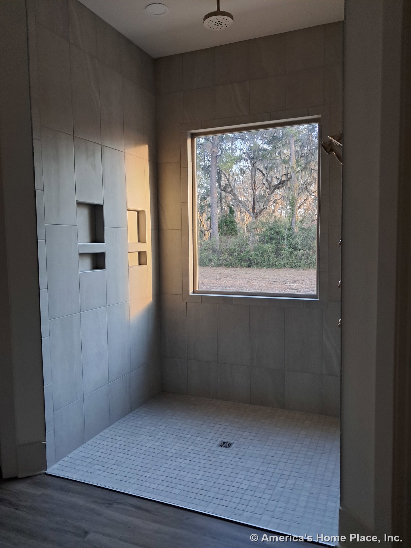 Walk-in shower with large format wall tiles, built-in shower niches, ceiling-mounted rain showerhead, square tile floor, picture window, and modern trim detailing.