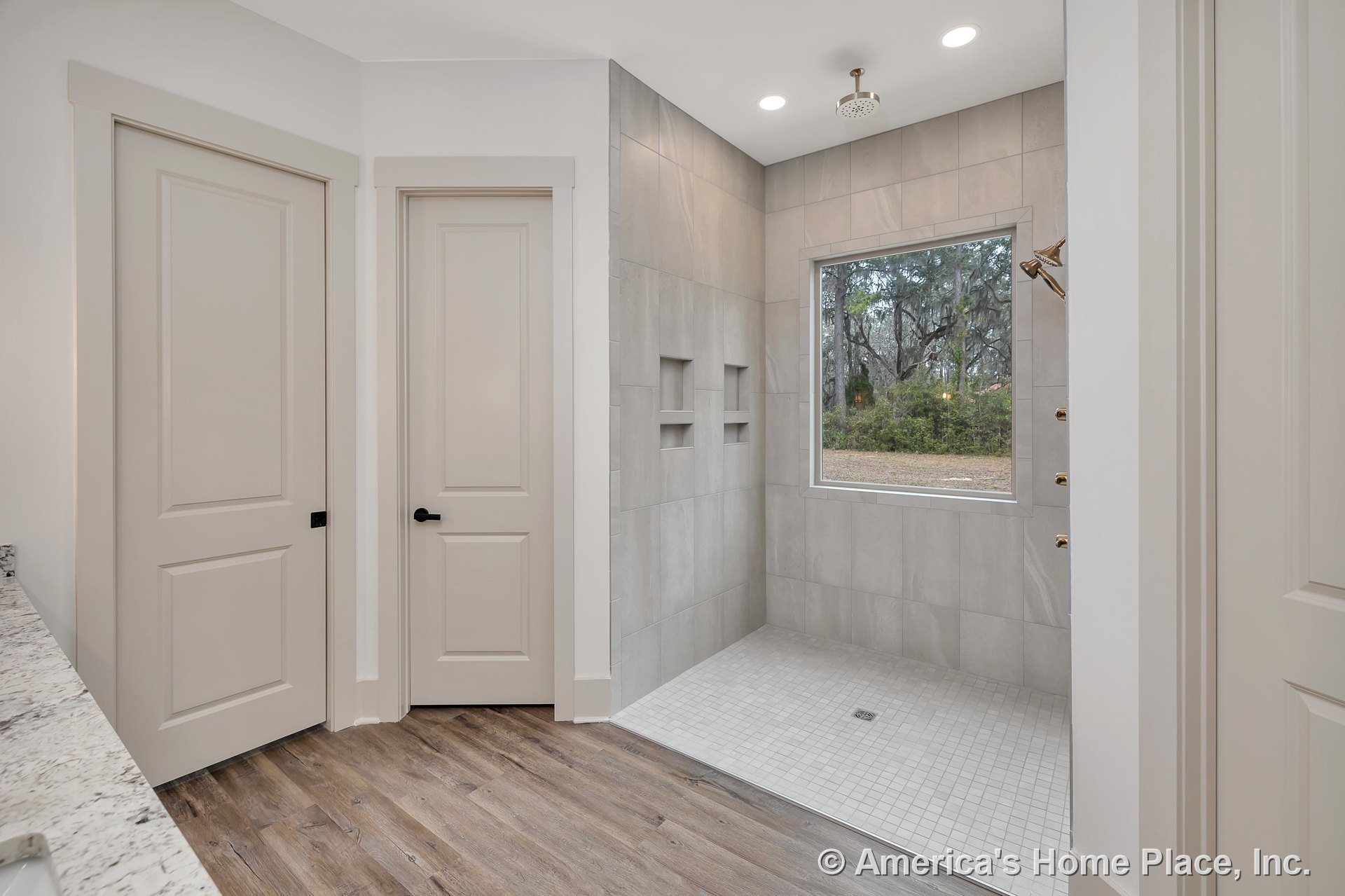 Spacious bathroom with walk-in tiled shower featuring built-in niches, large window in shower area, recessed ceiling lights, marble countertop, wood-look flooring, and modern
