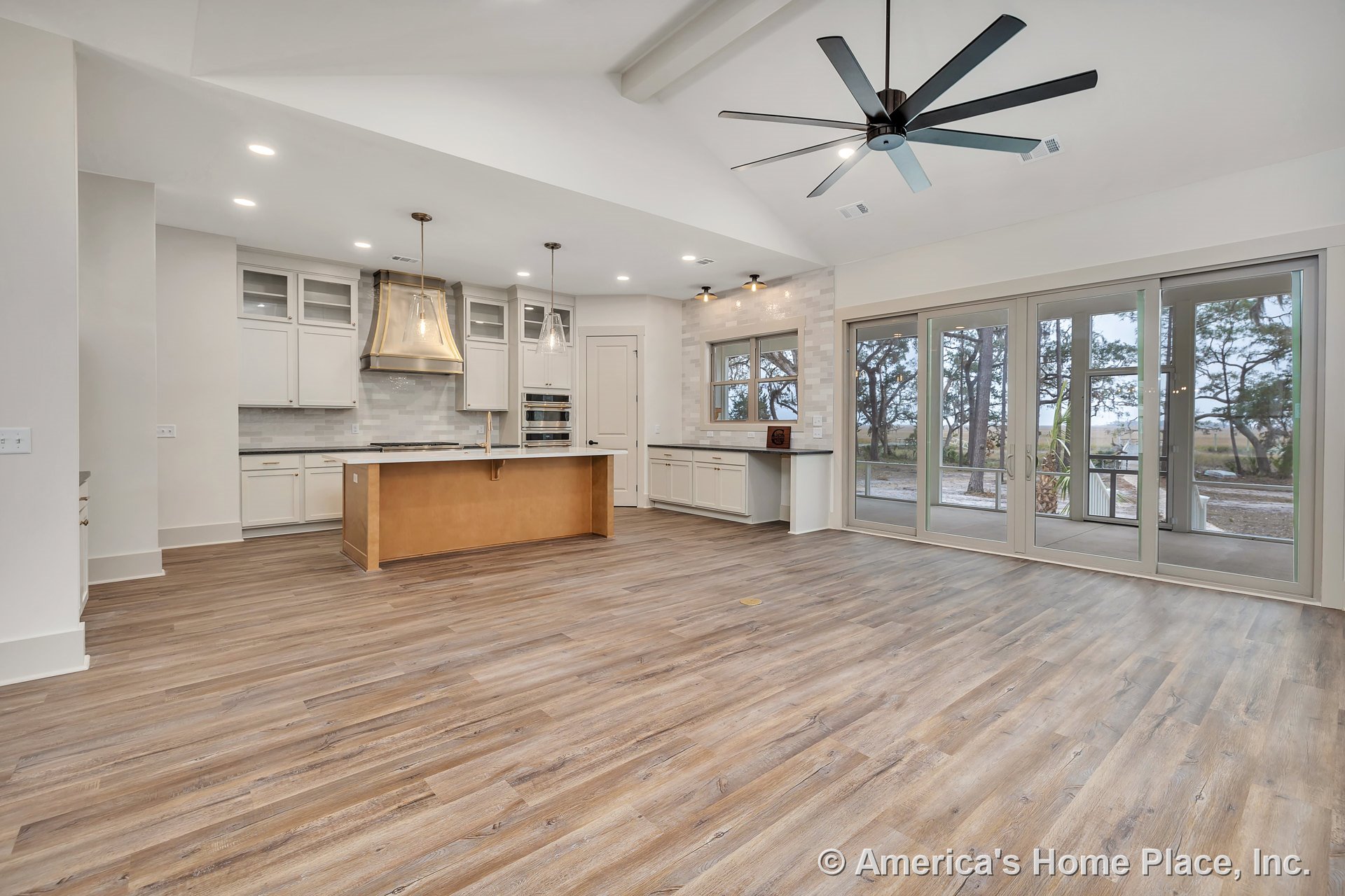 Open concept kitchen and living area with vaulted ceiling and exposed beam, wide plank wood flooring, glass-front kitchen cabinets, stainless steel range hood, tile backsplash