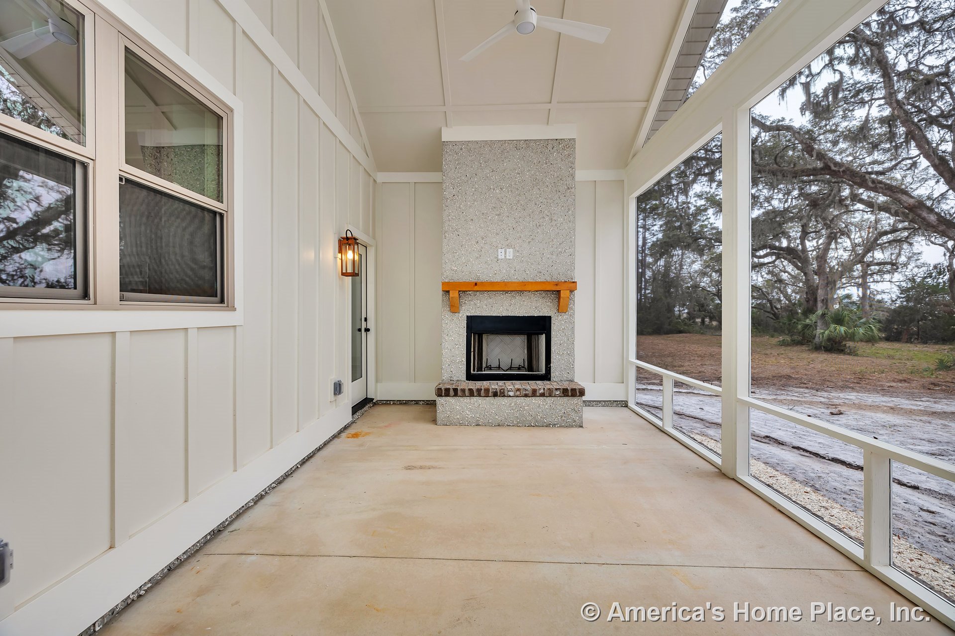 Screened porch with built-in fireplace featuring a wood mantel and brick hearth, concrete flooring, ceiling fan, exterior lighting, panel siding, windows, and glass door with trim.