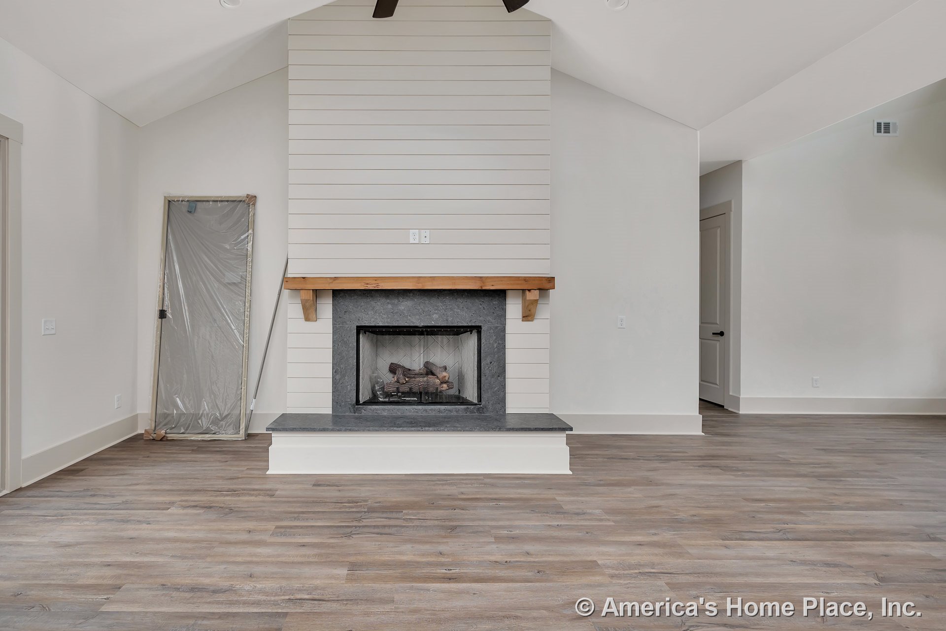 Shiplap accent wall with built-in stone fireplace, wood mantel, vaulted ceiling, wide plank wood flooring, and neutral trim and baseboards.