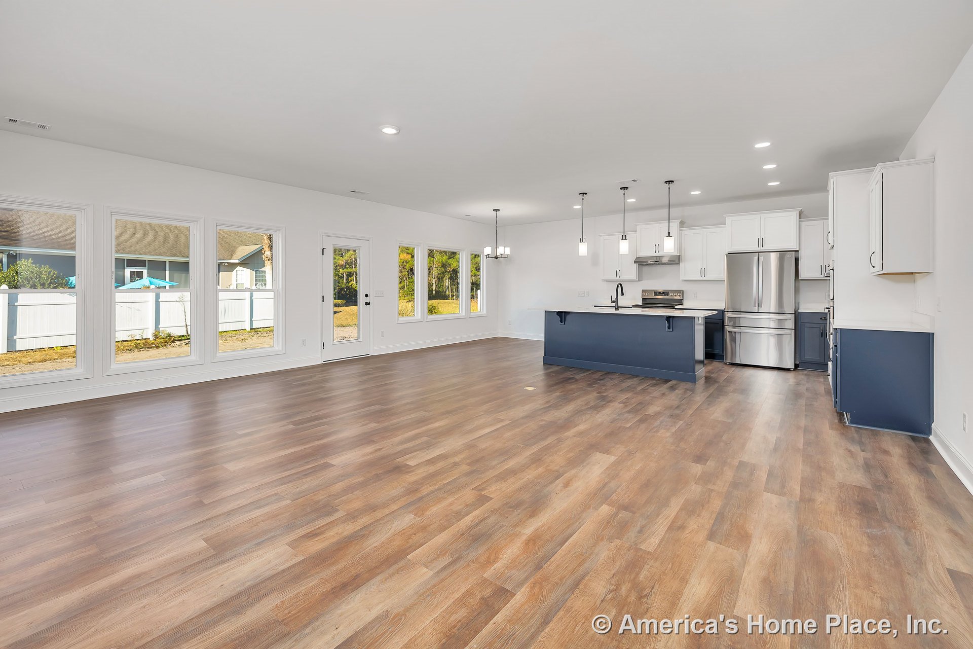 Open-concept kitchen and living area with wide plank wood-look vinyl flooring, white shaker cabinets, navy blue kitchen island, stainless steel appliances, pendant and recessed