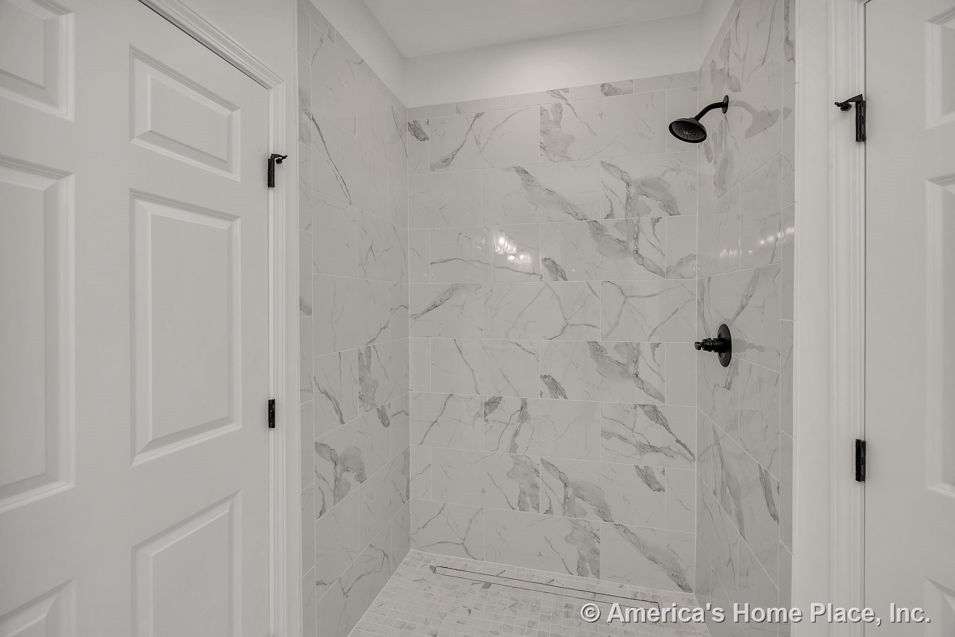 Walk-in shower with large-format marble-look tile walls, matte black shower fixtures, linear floor drain, and white paneled doors; modern built-in finishes throughout.