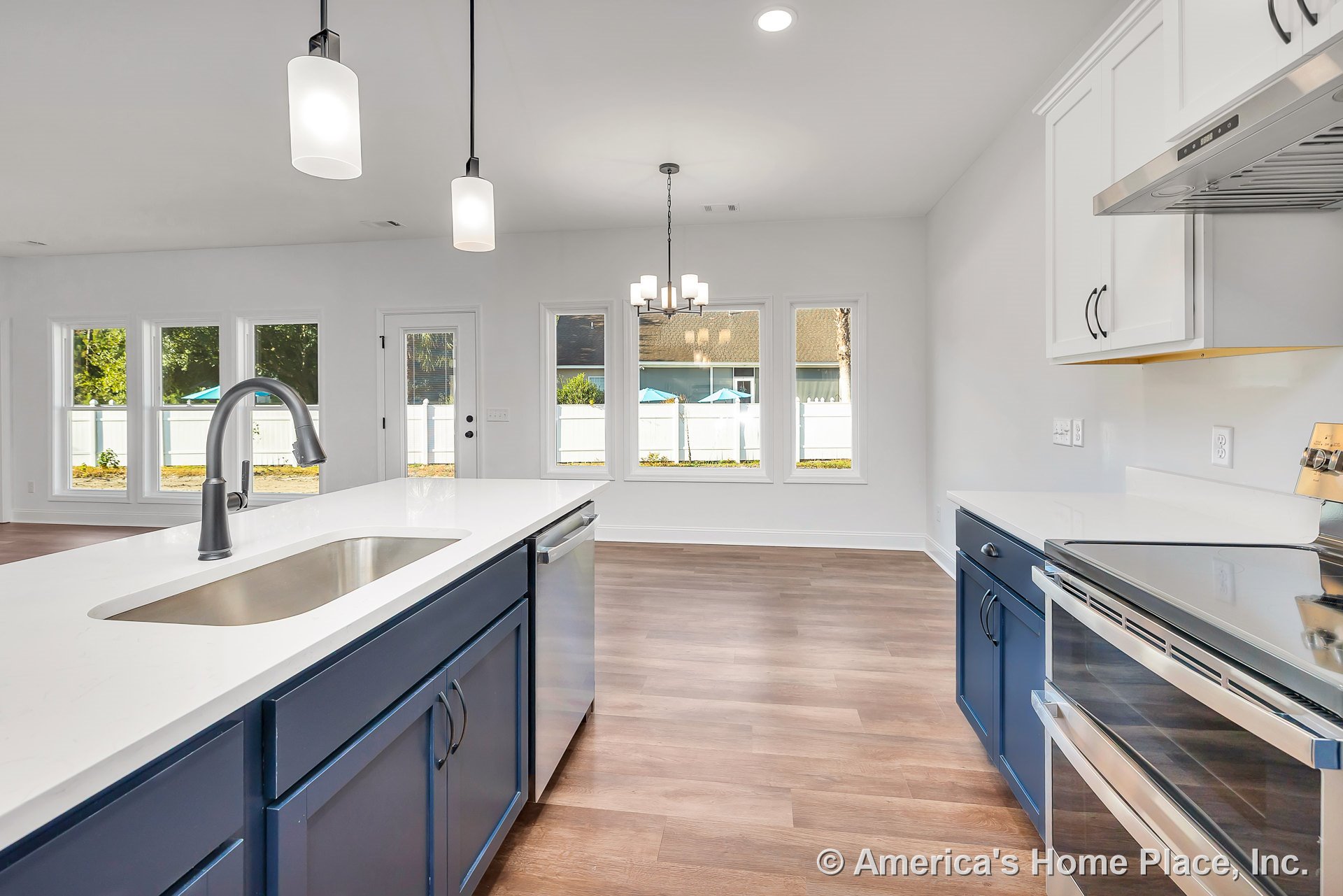Blue lower cabinets and white upper cabinets with quartz countertops, stainless steel appliances, wide stainless sink, pendant lights above kitchen island, wood-look flooring