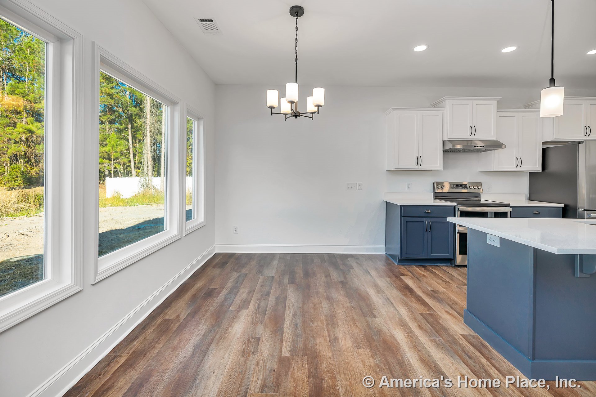 Spacious kitchen and dining area with three large picture windows, white upper cabinets, blue lower cabinets and island, stainless steel appliances, wood-look plank flooring, and
