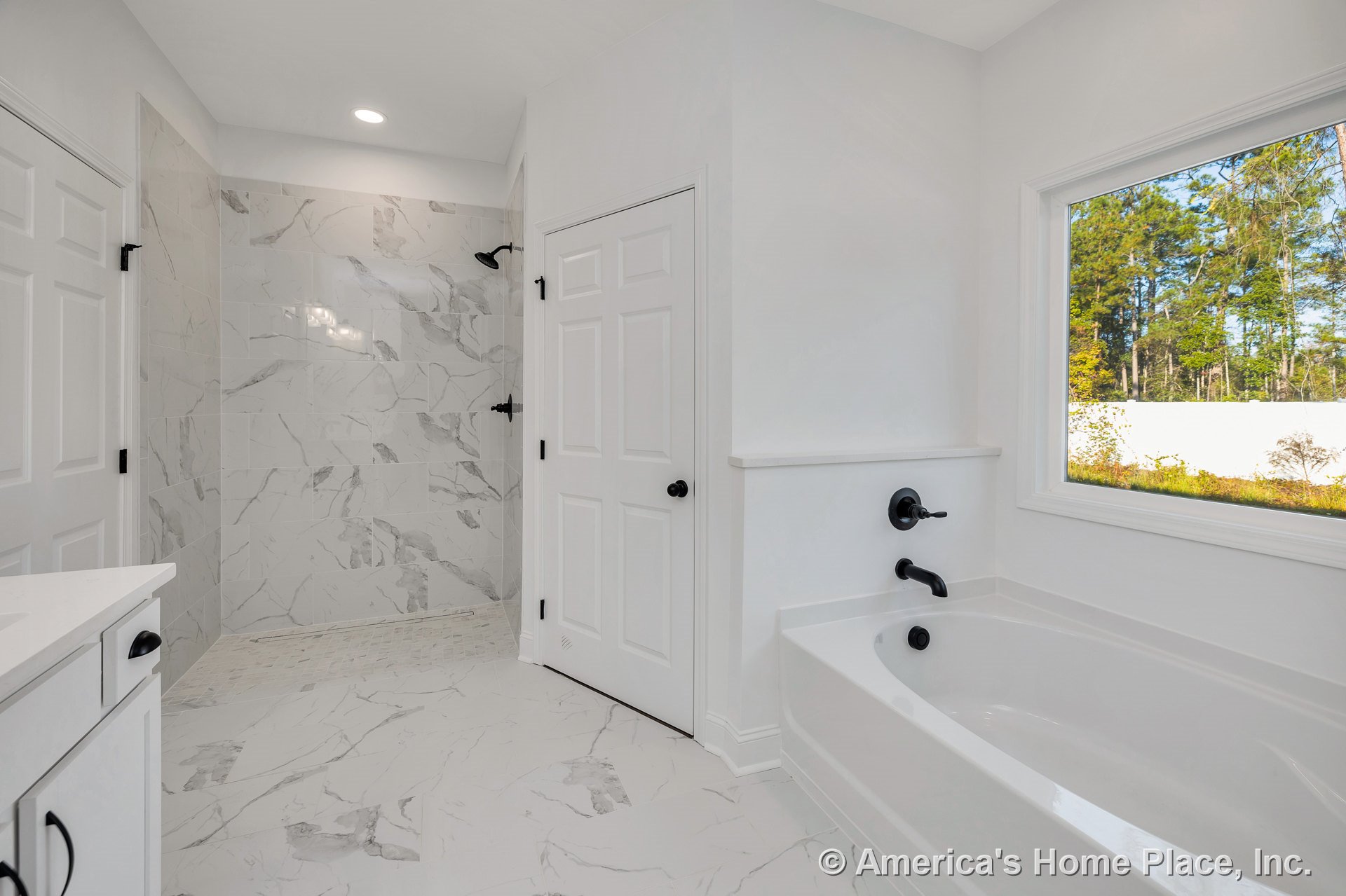 Walk-in shower with large marble-look tile, white soaking tub beneath a picture window, black plumbing fixtures, white cabinetry, recessed ceiling light, tile flooring, modern