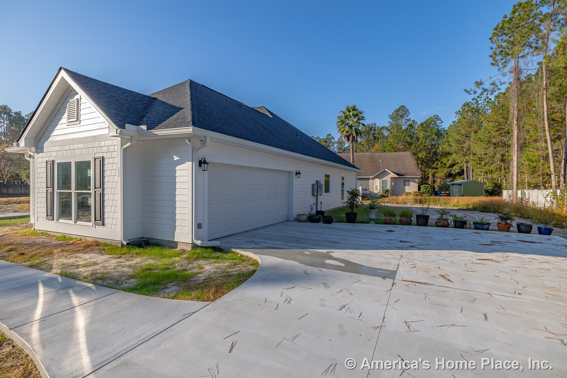 Two-car garage with white horizontal siding, architectural roof shingles, decorative window shutters, concrete driveway, exterior wall lanterns, and large front windows.