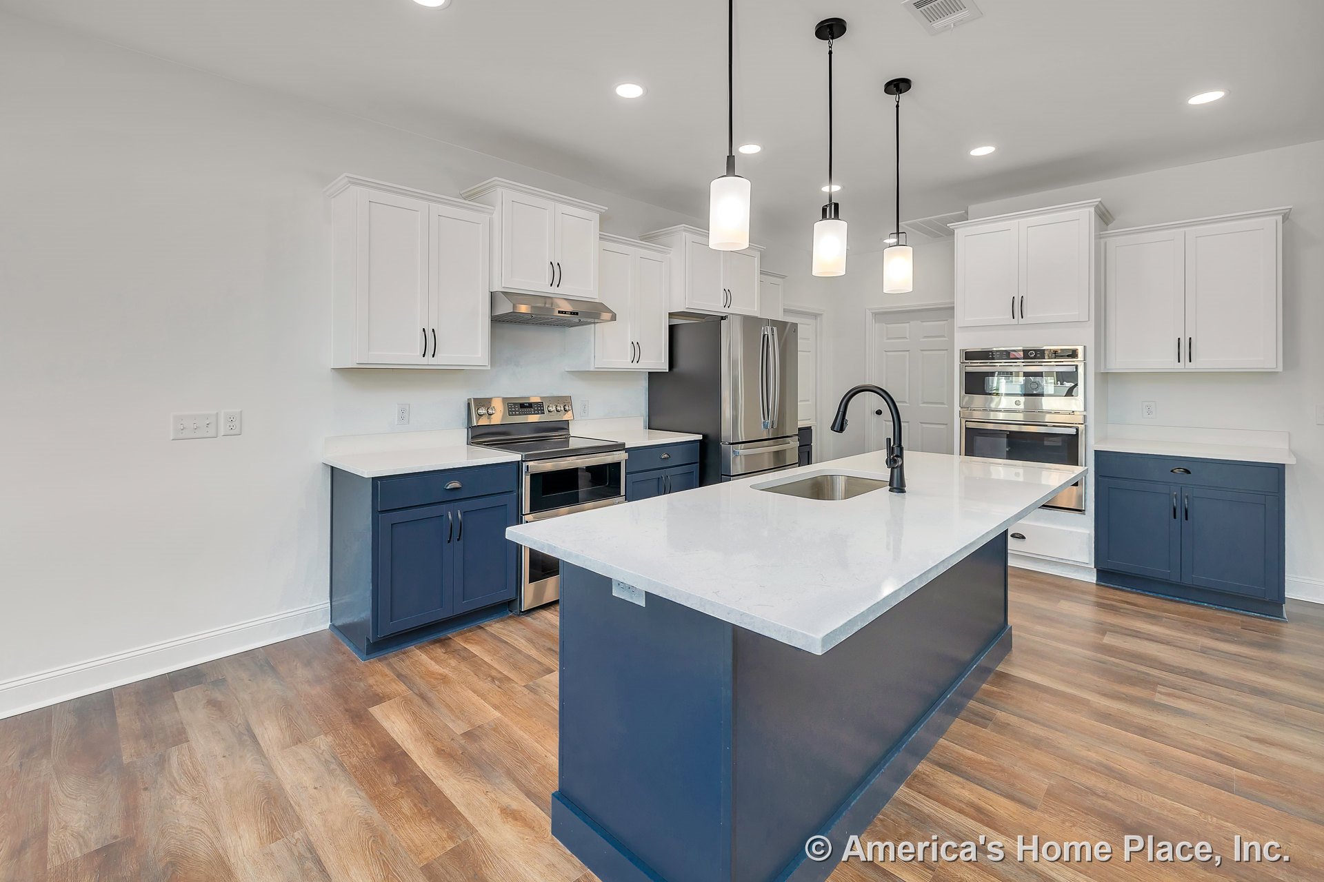 Large kitchen island with white quartz countertops, navy lower cabinets, white upper cabinets, stainless steel double oven, modern range hood, pendant and recessed lighting