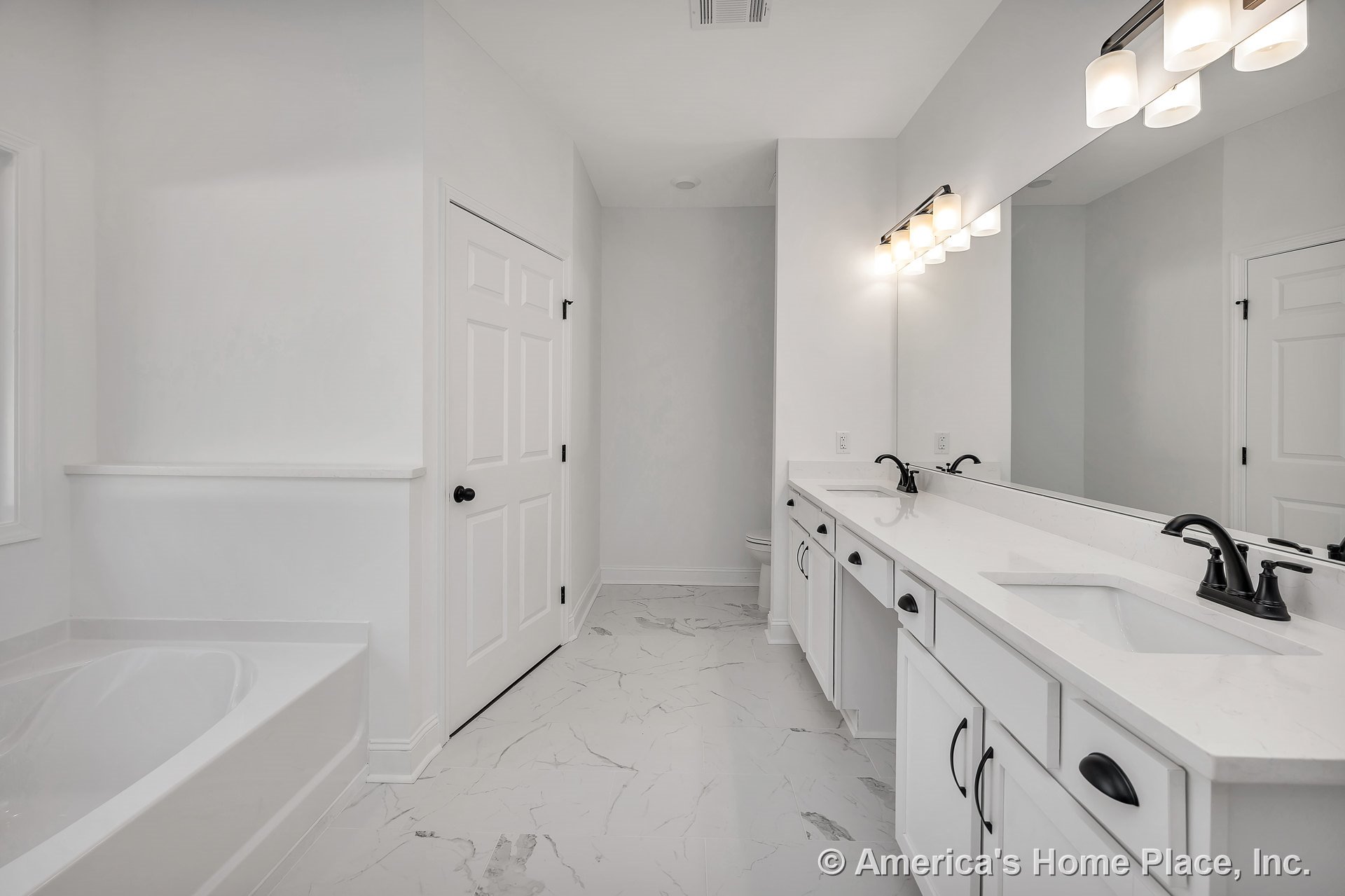 Double vanity with white shaker cabinets, quartz countertops, marble-look tile flooring, built-in bathtub, wall-mounted vanity lighting, large mirror, and black hardware.