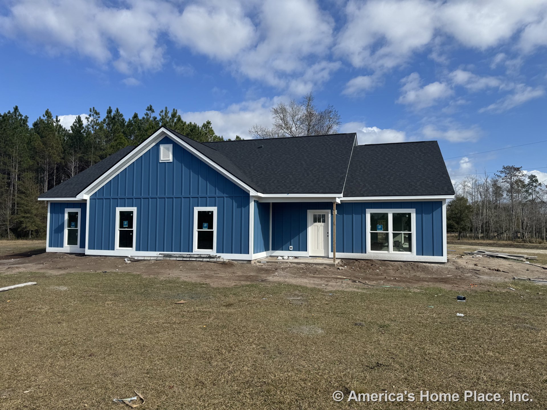 Blue vertical siding with white trim accents, black shingle gable roof, multiple rectangular windows, covered entry porch, and gable vent on new residential construction exterior.