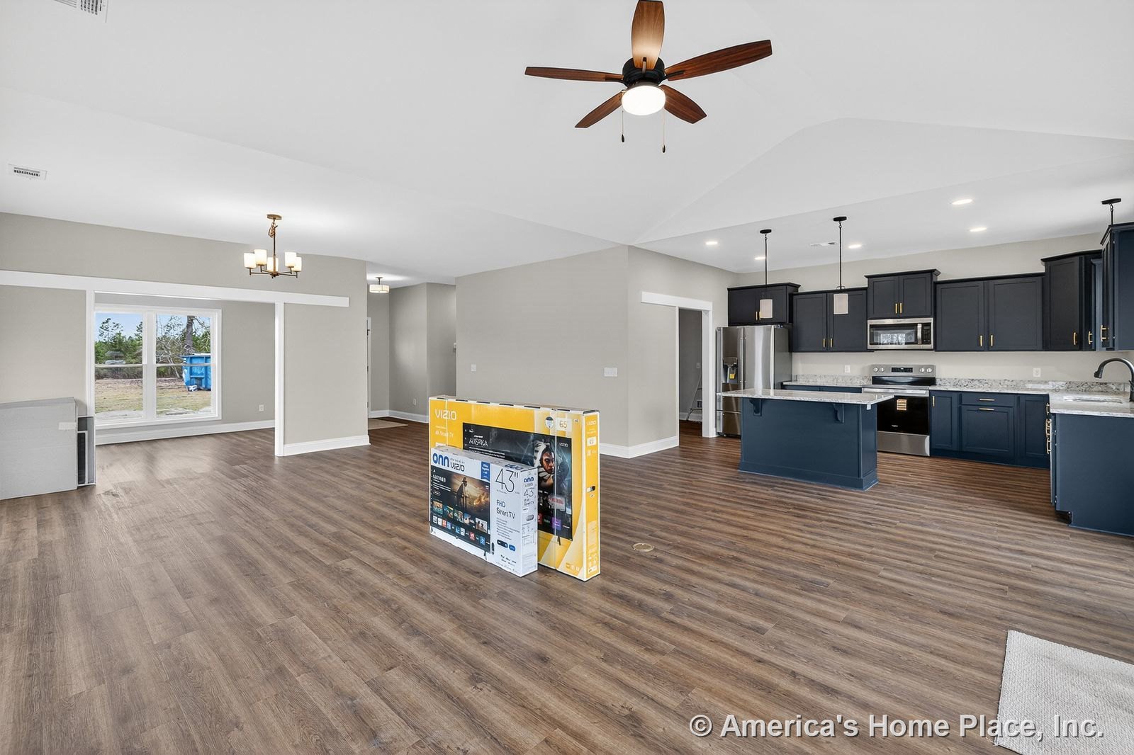 Open concept kitchen with navy cabinetry, granite countertops, stainless steel appliances, vaulted ceiling with ceiling fan, pendant lights above the island, built-in microwave and