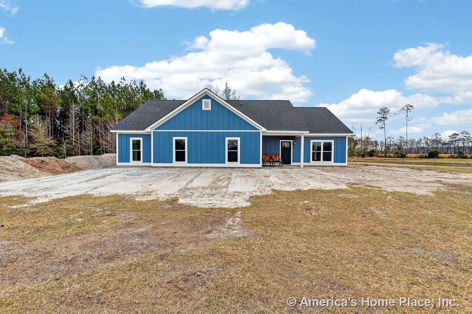 Blue vertical panel siding with white trim, symmetrical placement of large windows, covered front porch, black shingle roof, and concrete driveway on a single-story residential
