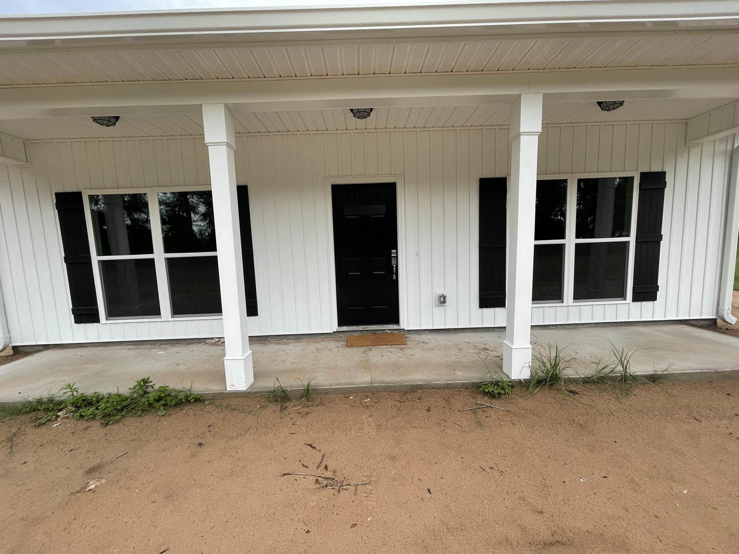 White siding home with black framed doors, covered porch, white columns, and concrete walkway