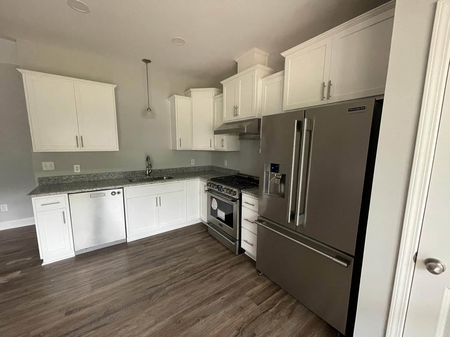 White kitchen cabinets with silver handles, stainless steel refrigerator with water dispenser, built-in oven, stove, dishwasher, light countertops, and tile flooring