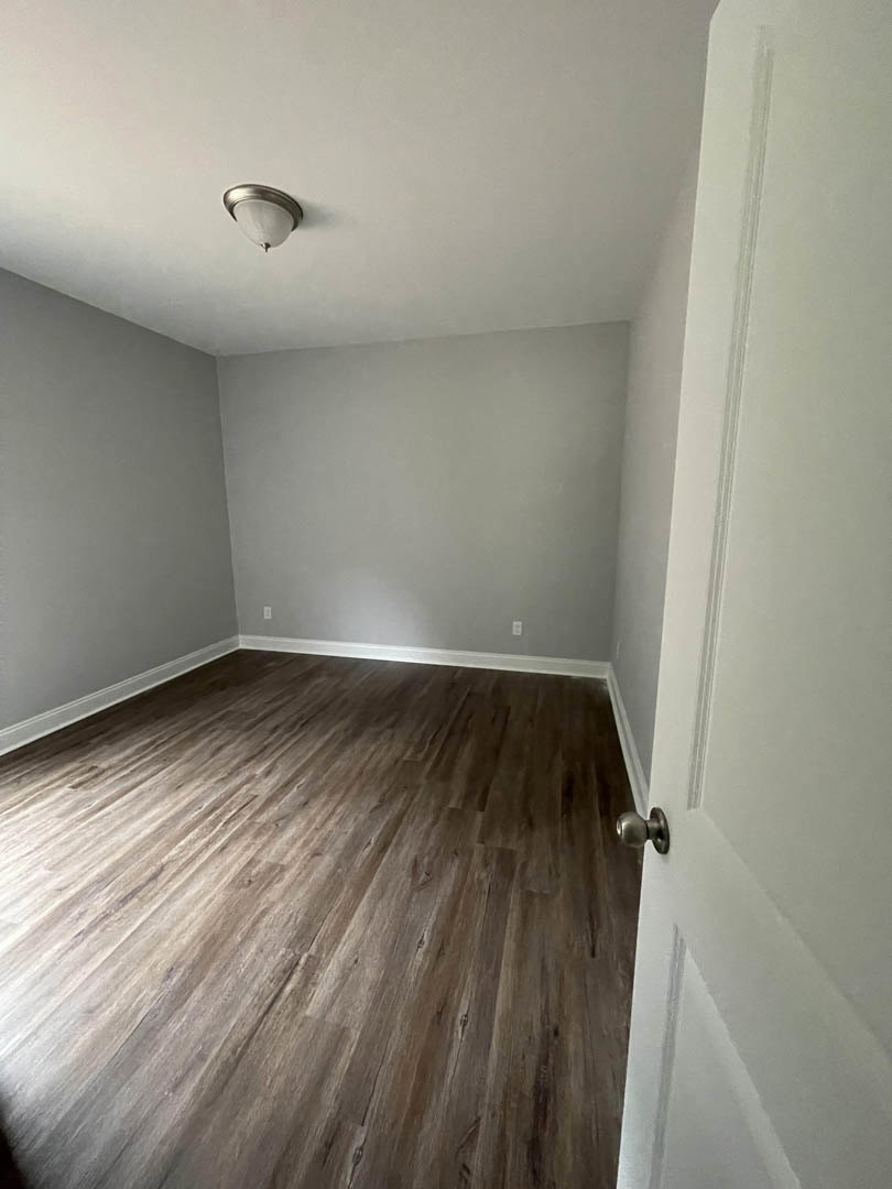 Wood flooring in a room with white plaster walls, modern ceiling light fixture, and a close-up view of a metal door knob