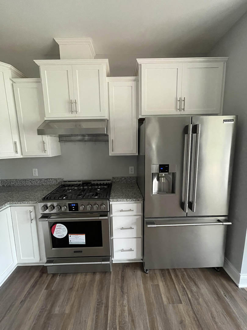 White kitchen cabinets with metal handles, stainless steel refrigerator, wood flooring, and stone countertops