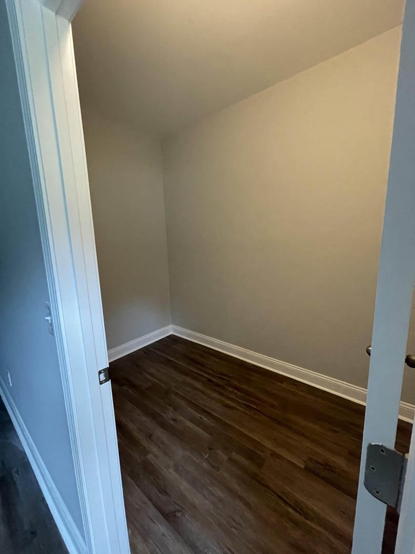 Wood flooring in a room with white plaster walls and an open door leading to another space