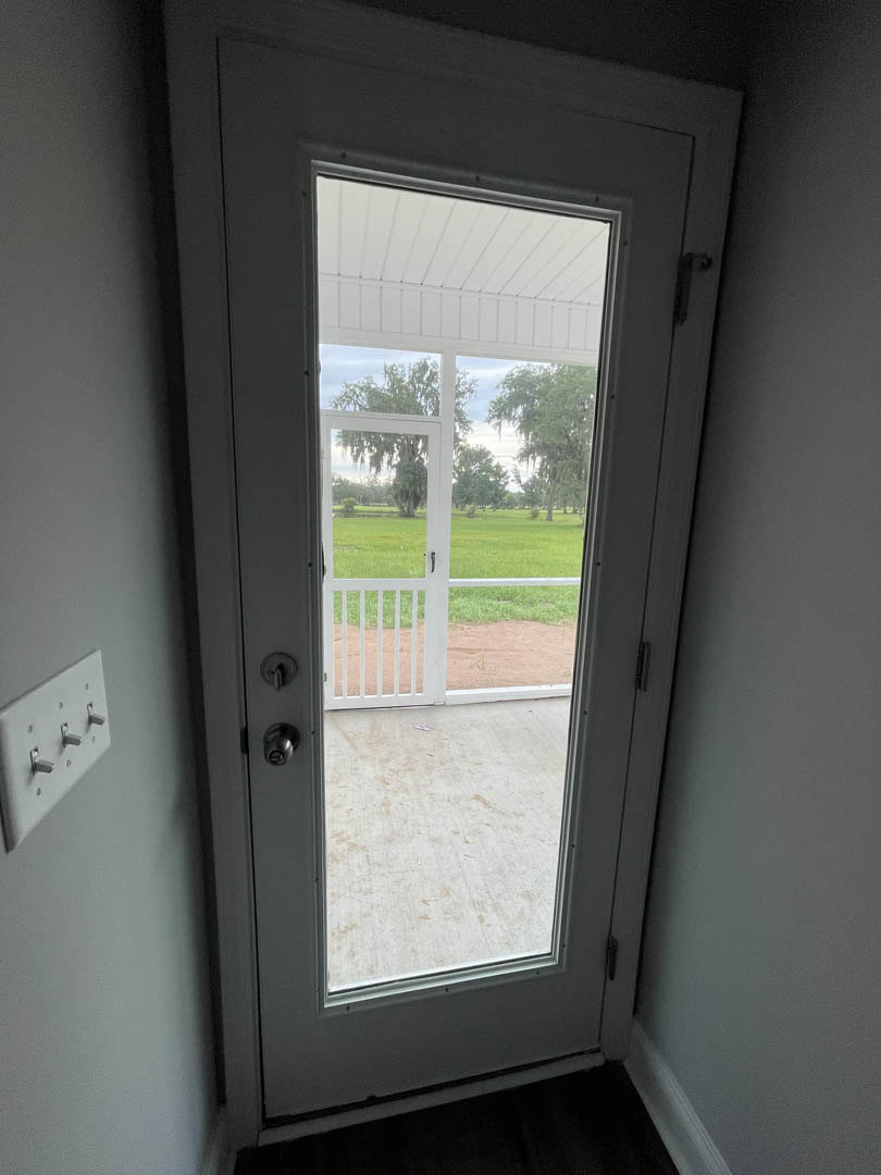 White entry door with glass panel, adjacent white fence, green grass lawn, and visible door handle