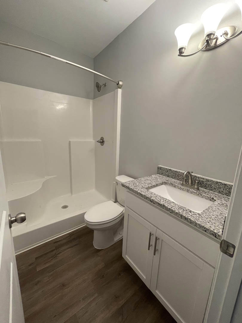 Modern bathroom featuring white tile flooring, a sleek toilet, white vanity with silver handles, undermount sink, chrome faucet, and a contemporary light fixture above.