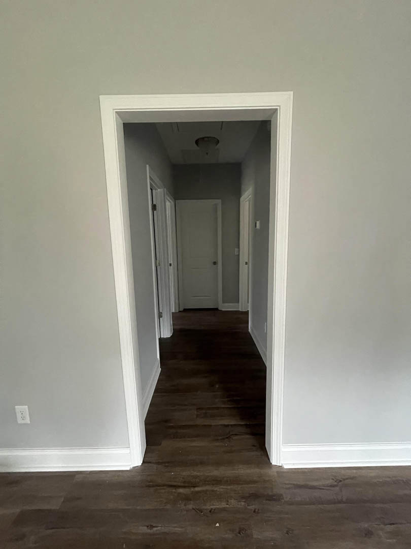 Hallway with white walls, white trim, and dark wood flooring, featuring white doors with black handles