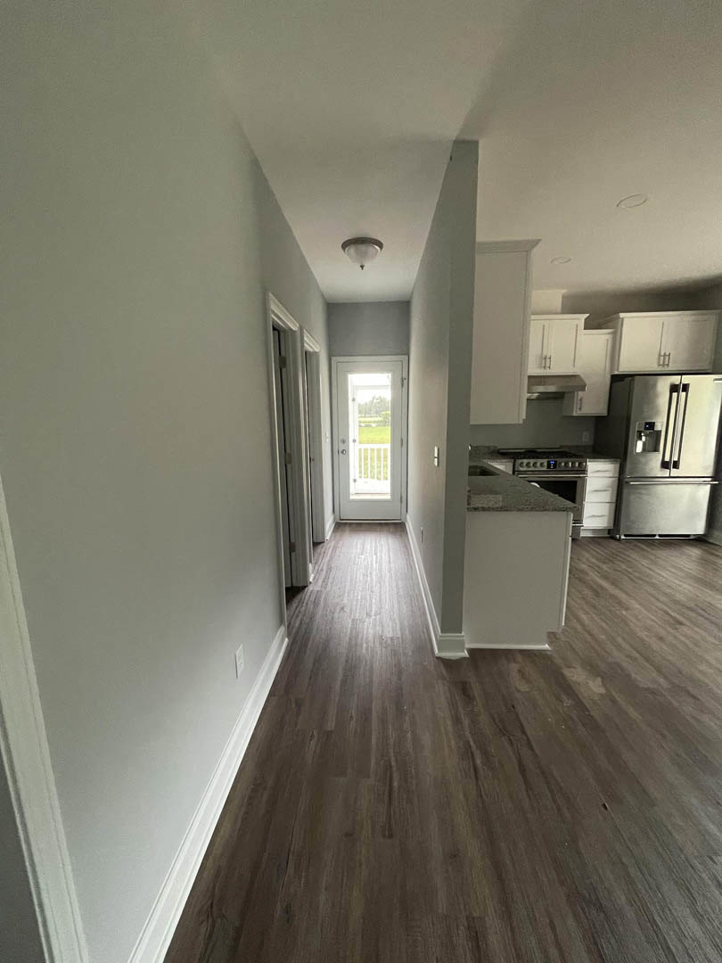 Open kitchen and dining area featuring hardwood floors, stainless steel refrigerator, white cabinetry with black countertops, and a white door leading to a green lawn.