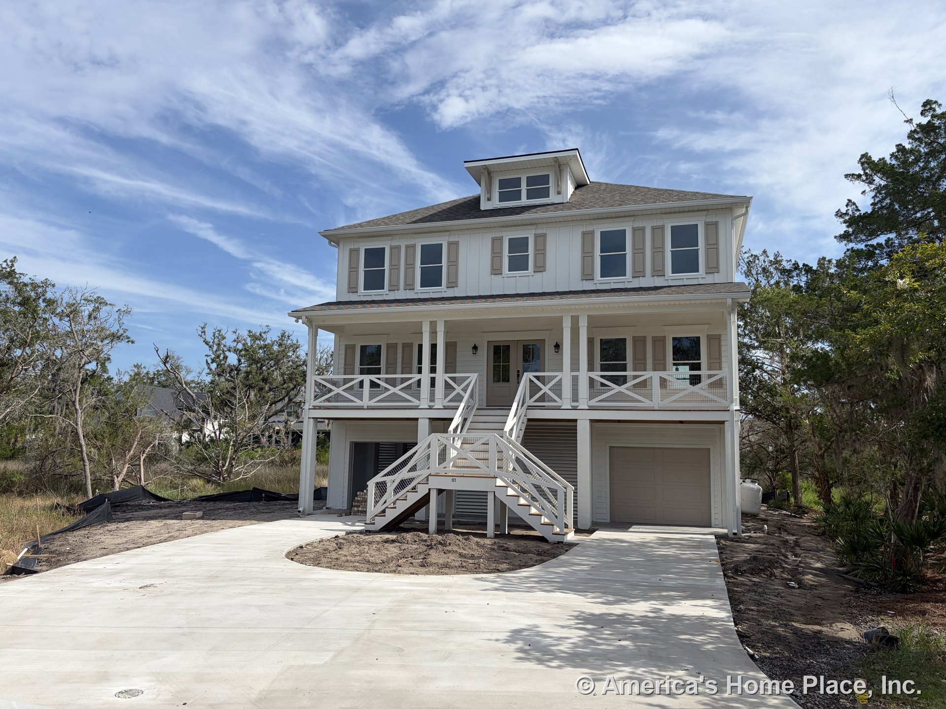 Two-story home with board and batten siding, covered front porch supported by columns and railing, attached garage, multiple double-hung windows with trim and shutters, concrete