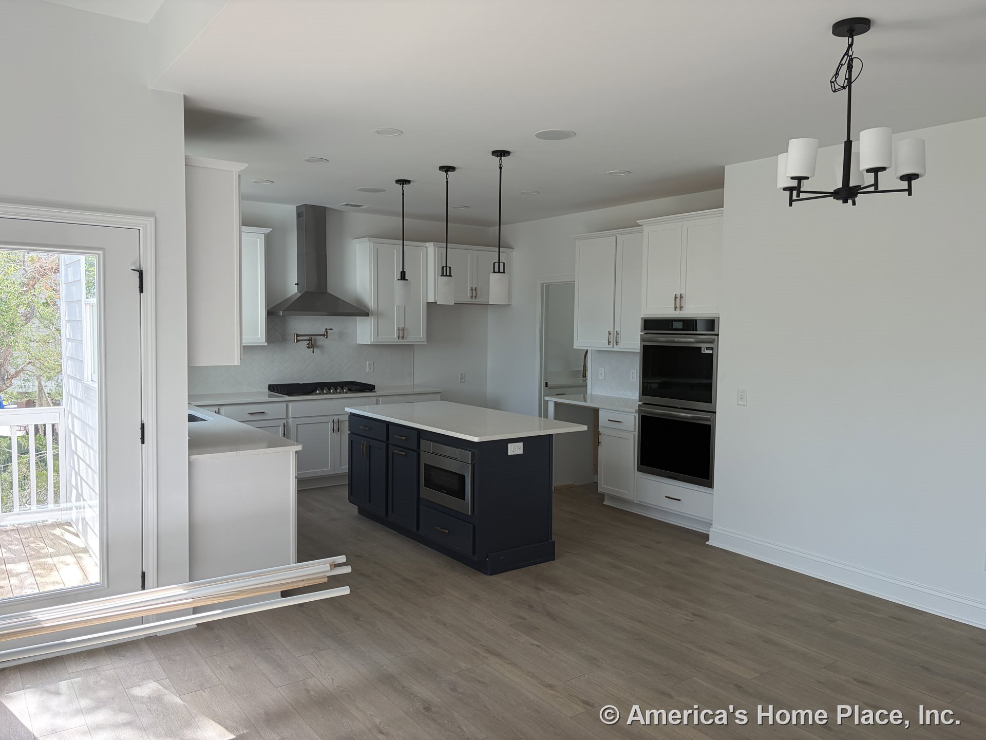Open kitchen with white shaker cabinets, navy island featuring built-in microwave, double wall ovens, pendant lights above island, wood-look flooring, tile backsplash, stainless