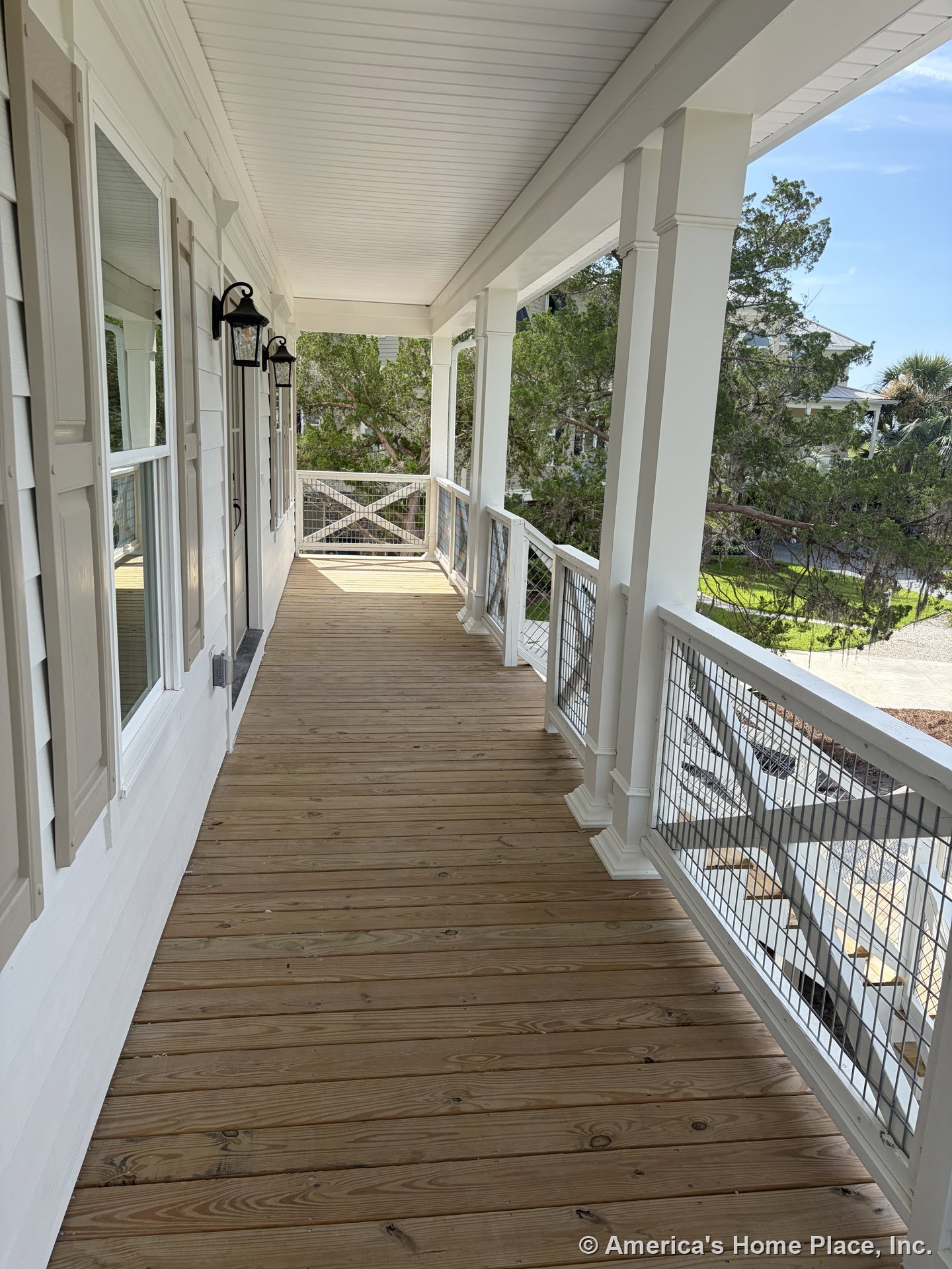 Covered porch featuring wood plank flooring, white railing with wire mesh, beige window shutters, exterior wall lanterns, column supports, and a tongue-and-groove ceiling.
