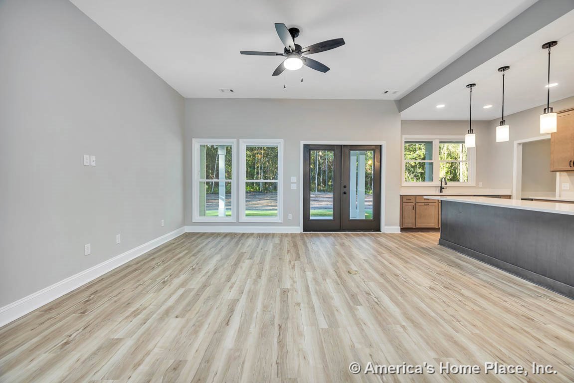 Open concept living area with light wood plank flooring, large picture windows, double glass exterior door, ceiling fan with light, kitchen peninsula featuring pendant lights, wood