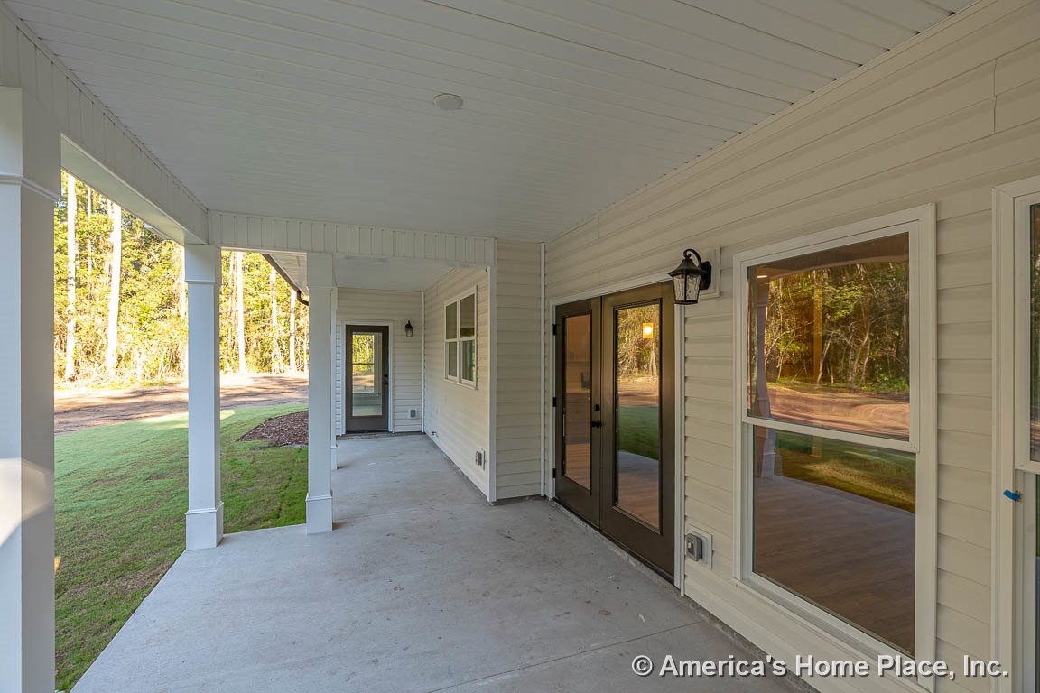 Covered front porch with concrete flooring, white vinyl siding, glass double doors, exterior windows, wall-mounted lantern light, decorative columns, and white trim.