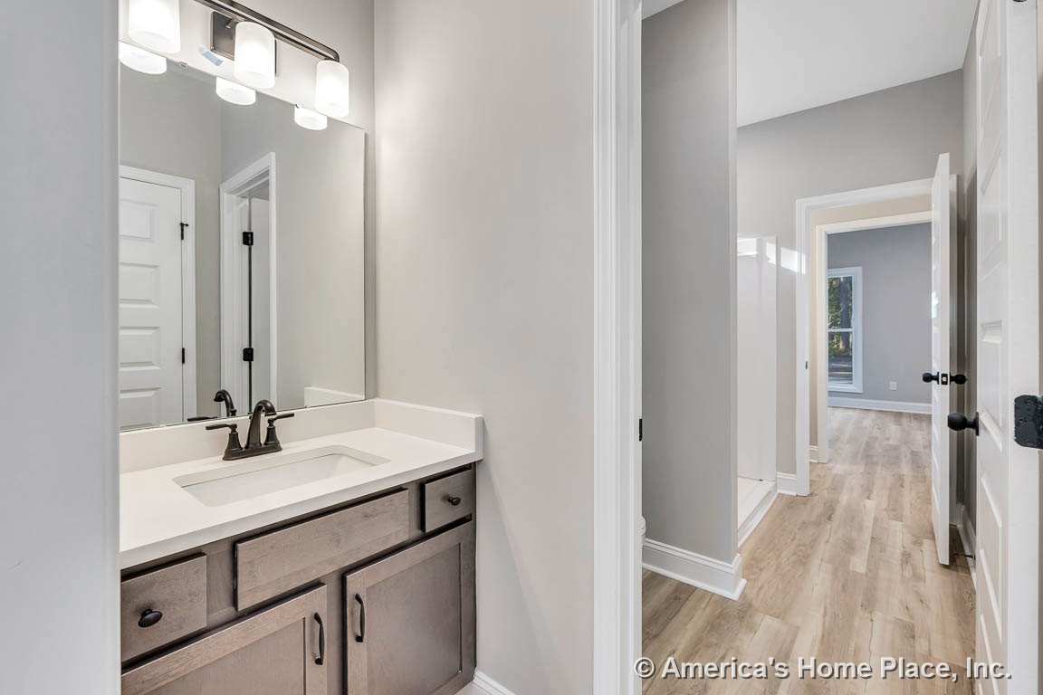 Single bathroom vanity with wood cabinetry and black hardware, quartz countertop with undermount sink, large wall mirror above, wall-mounted light fixture, white paneled doors and