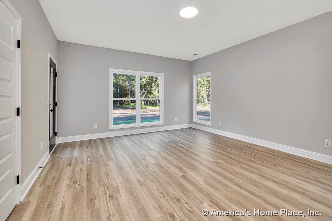 Living room with large double windows, light wood-look flooring, gray painted walls, white baseboards, recessed ceiling light, and paneled interior door.