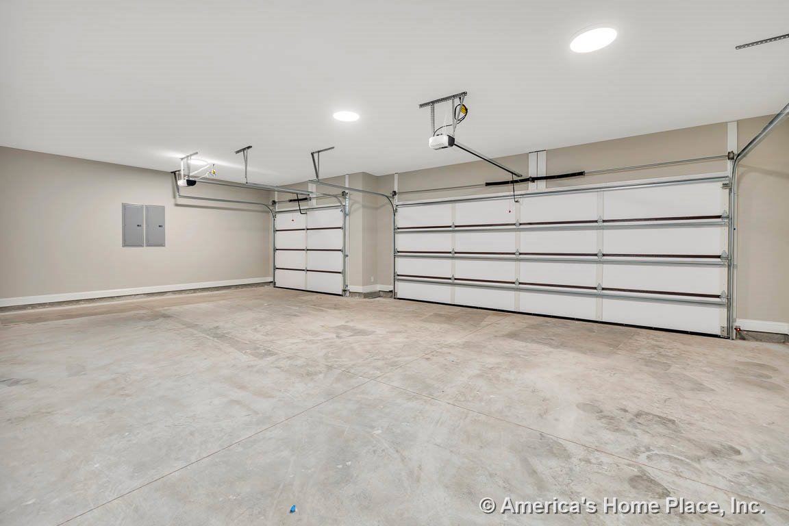 Spacious garage with three overhead doors, concrete flooring, recessed ceiling lights, wall-mounted electrical panels, neutral painted walls, and white baseboard trim.