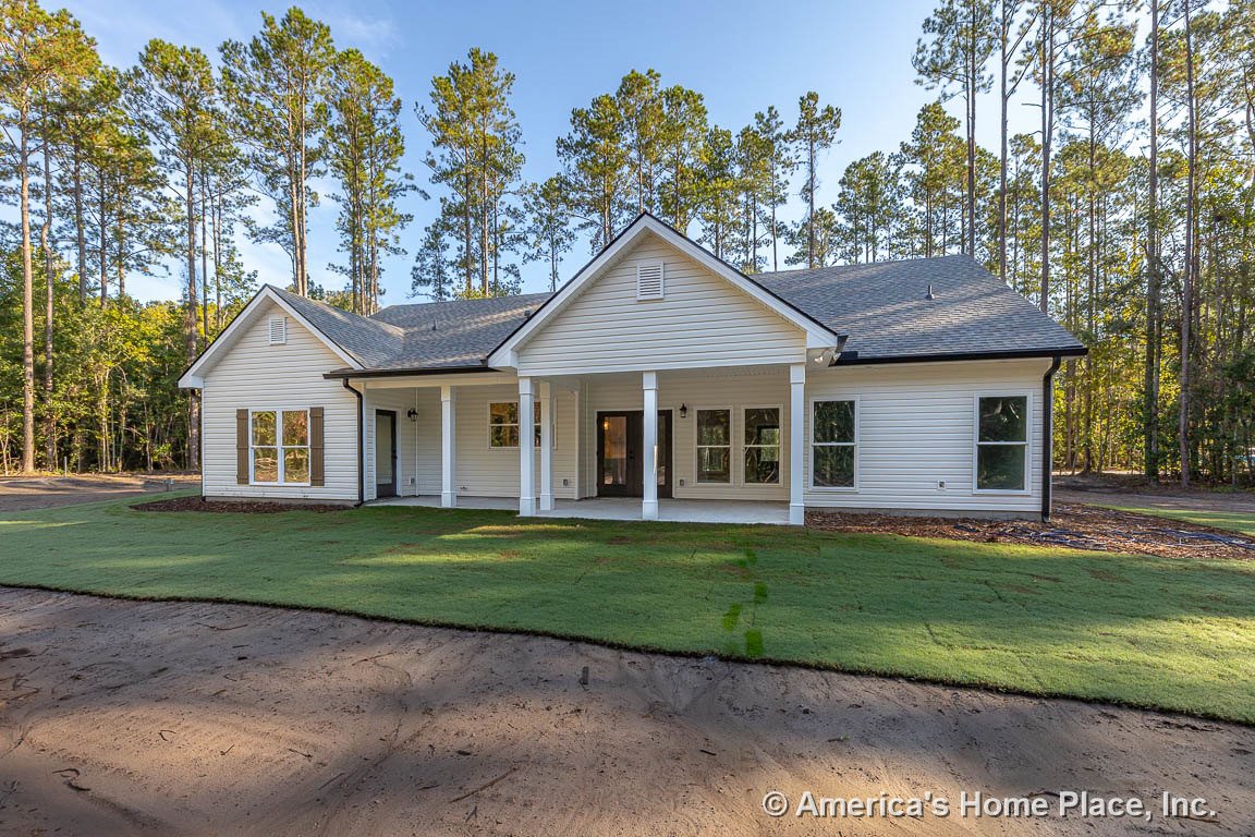 Covered front porch with white columns, white siding exterior, multiple double-hung windows with brown shutters, gable roof, and freshly laid sod lawn.
