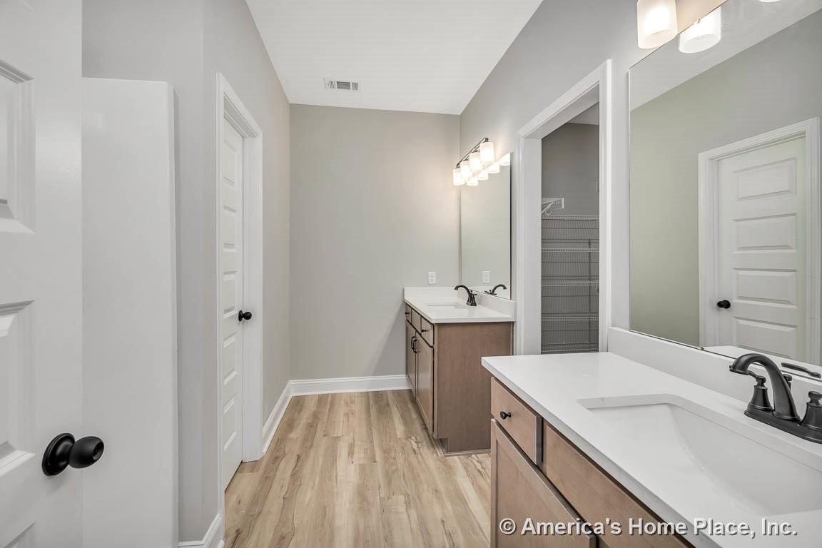 Dual vanities with white quartz countertops and wood base cabinets, large wall mirrors above each sink, modern light fixtures, built-in shelving, light wood flooring, and white