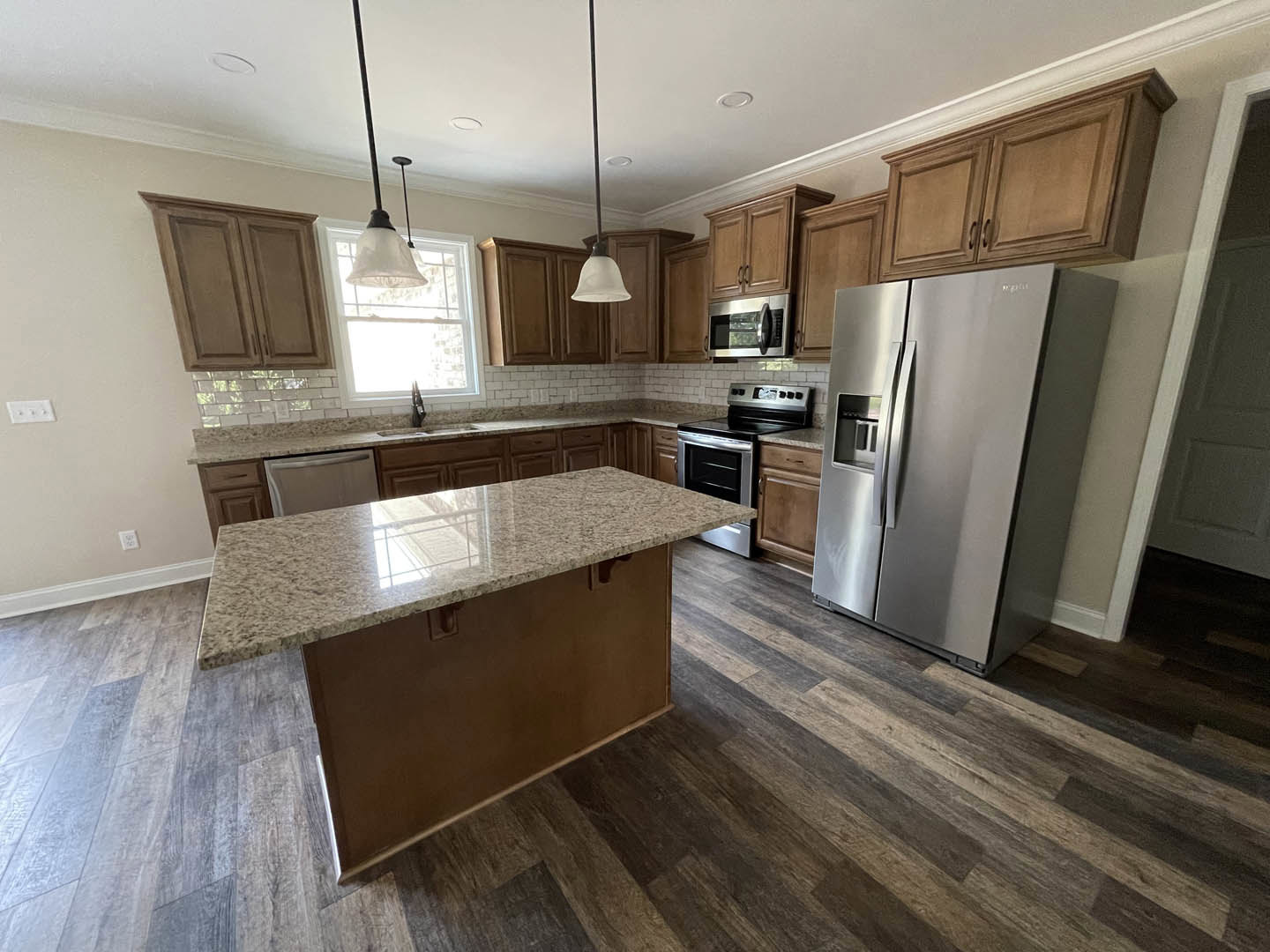 Kitchen with marble-topped island, stainless steel refrigerator, tile backsplash, granite countertops, white cabinetry, built-in microwave, stove and oven, pendant light fixture