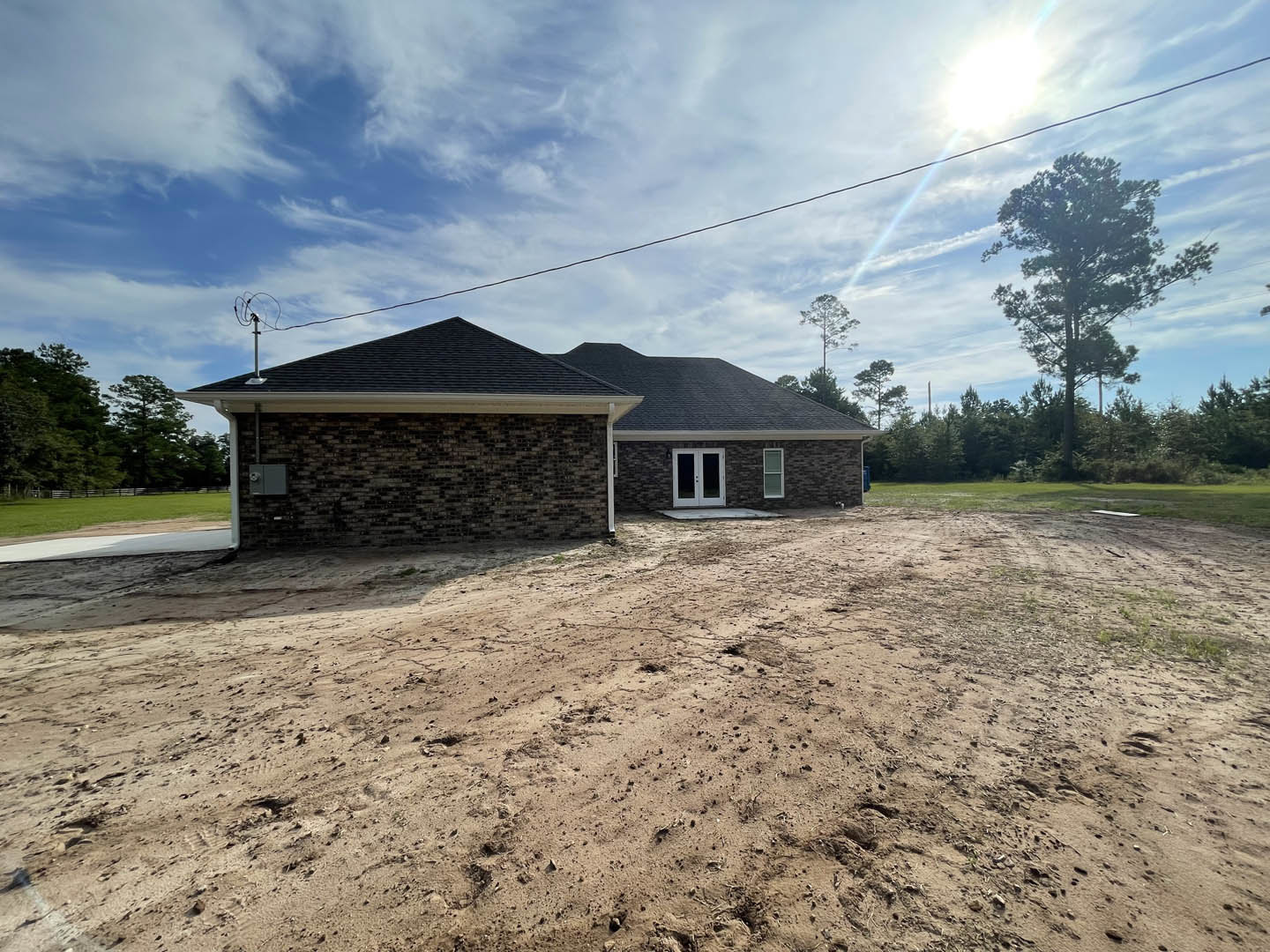 White-roofed house with double glass doors, surrounded by dirt field and tall tree, power lines overhead, Plattsburgh Air Force Base visible in distant background