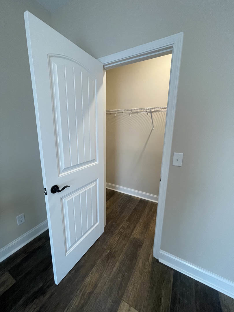 White door open to a closet with white walls, wood flooring, and a white curtain rod above the closet opening