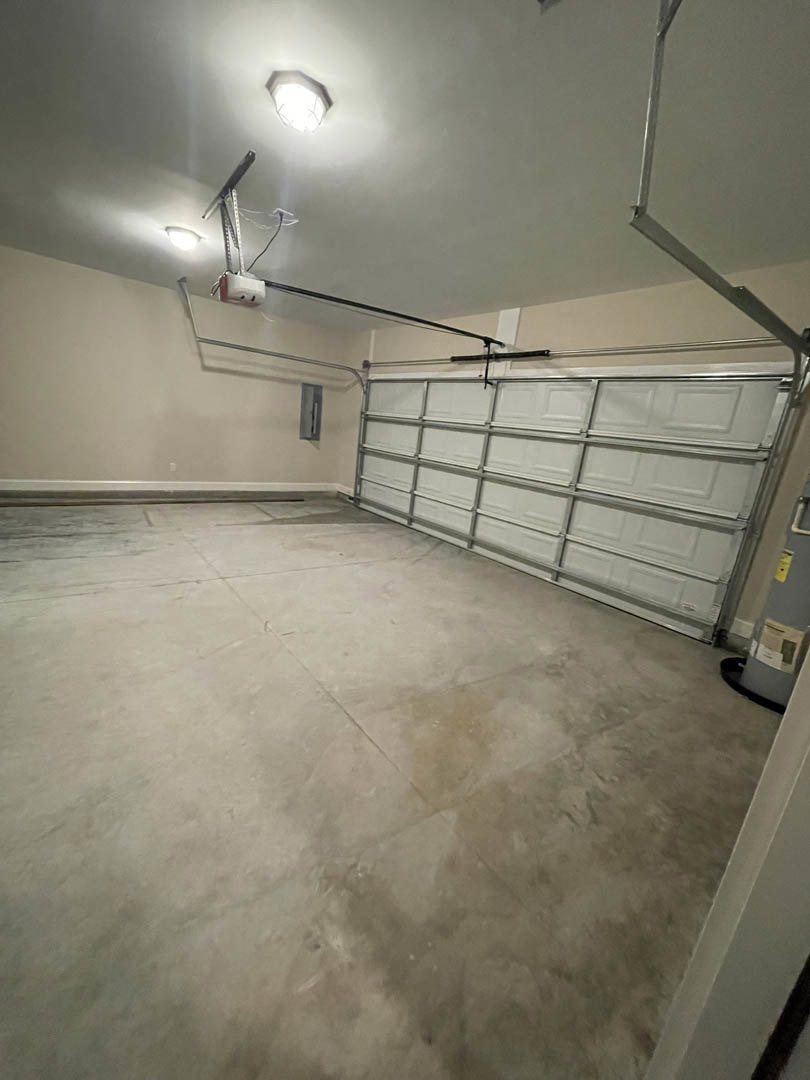 Garage interior with smooth white plaster walls, white ceiling, overhead light fixture, metal-framed garage door, and concrete flooring.