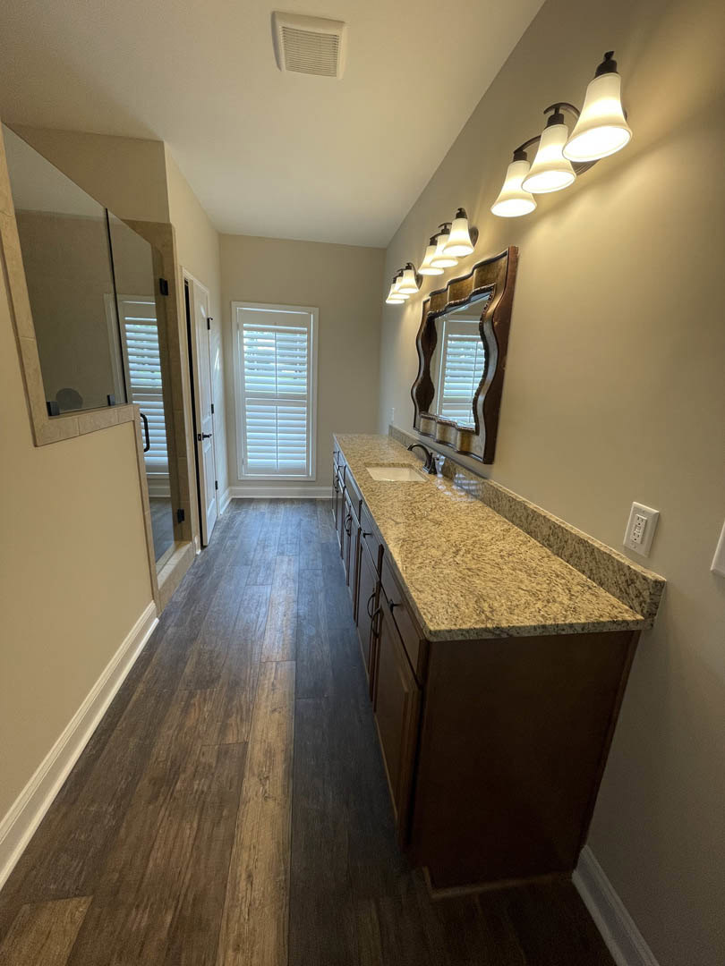 Bathroom with marble countertop, curved-edge mirror, window with blinds, ceiling vent, and close-up of modern light fixture