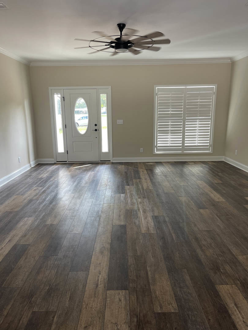 Wood flooring and white walls in a room with a ceiling fan, white door with window, and window shutter; window offers view of an airplane outside.